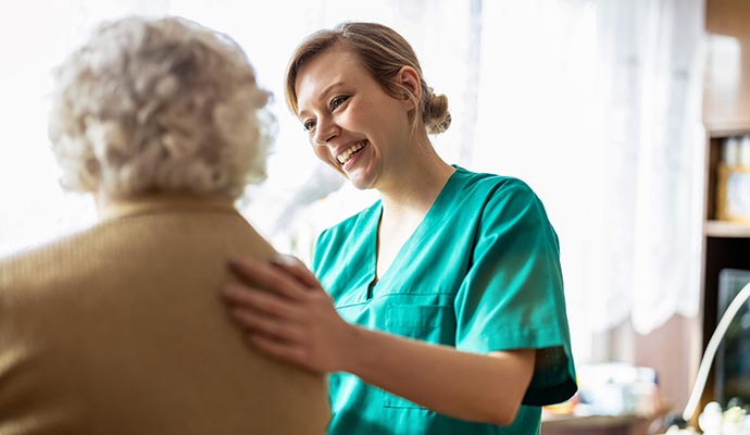 Smiling caregiver in green uniform supporting an elderly woman