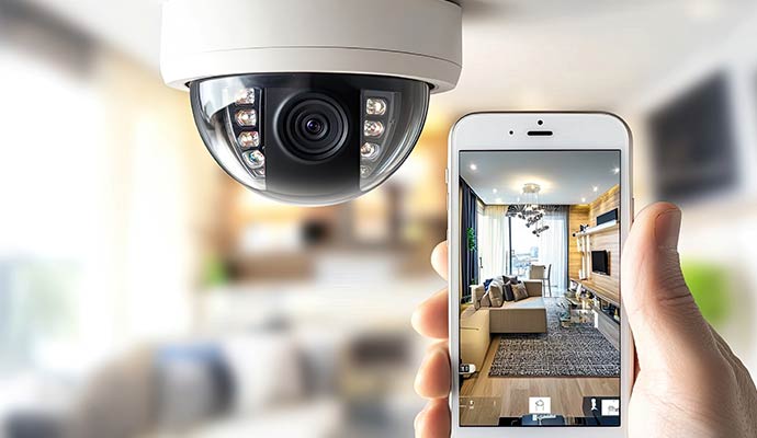 A dome security camera mounted on a ceiling next to a smartphone showing a live feed of a living room